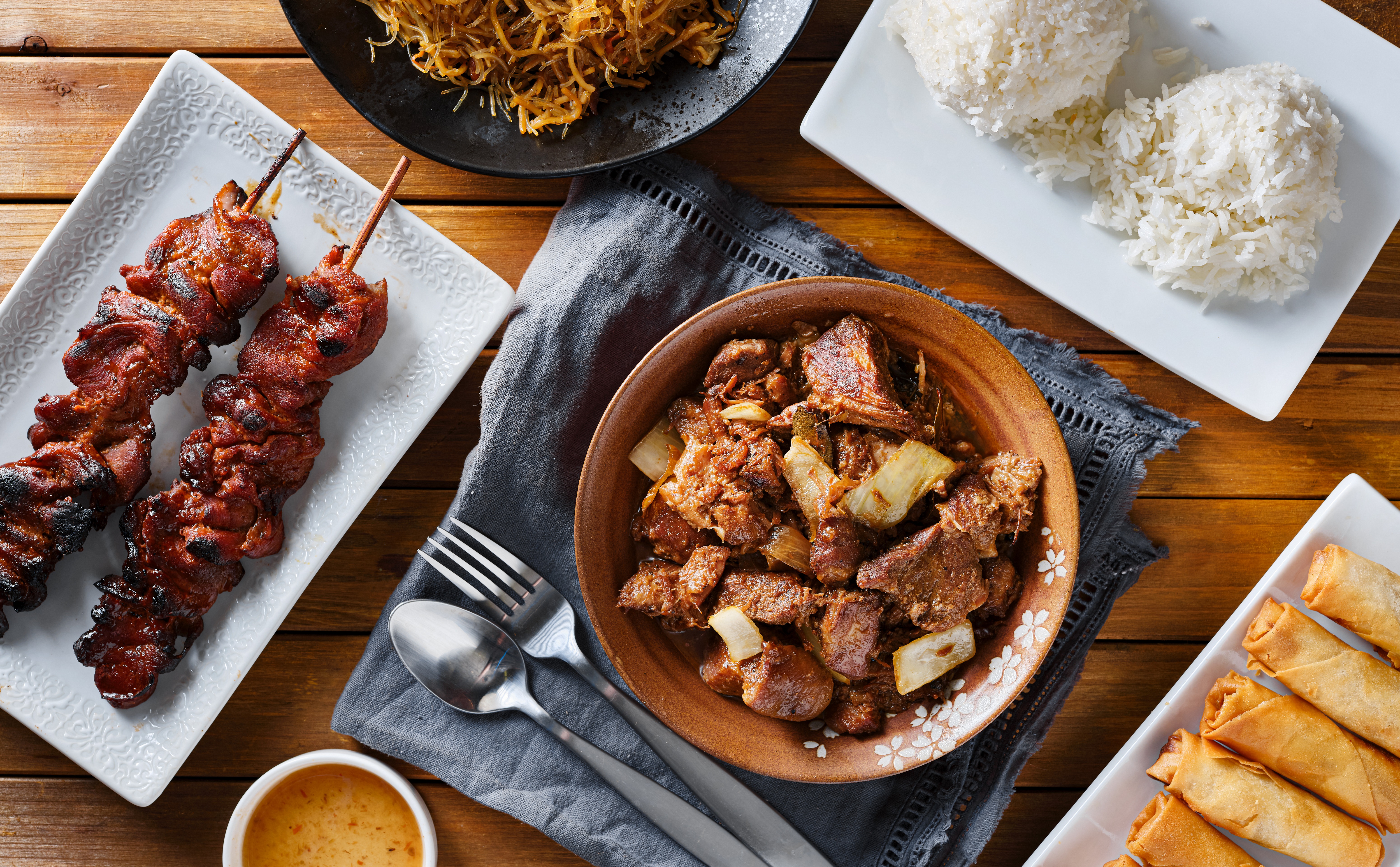 pork adobo meal with filipino foods such as lumpia, pancit noodles, and rice