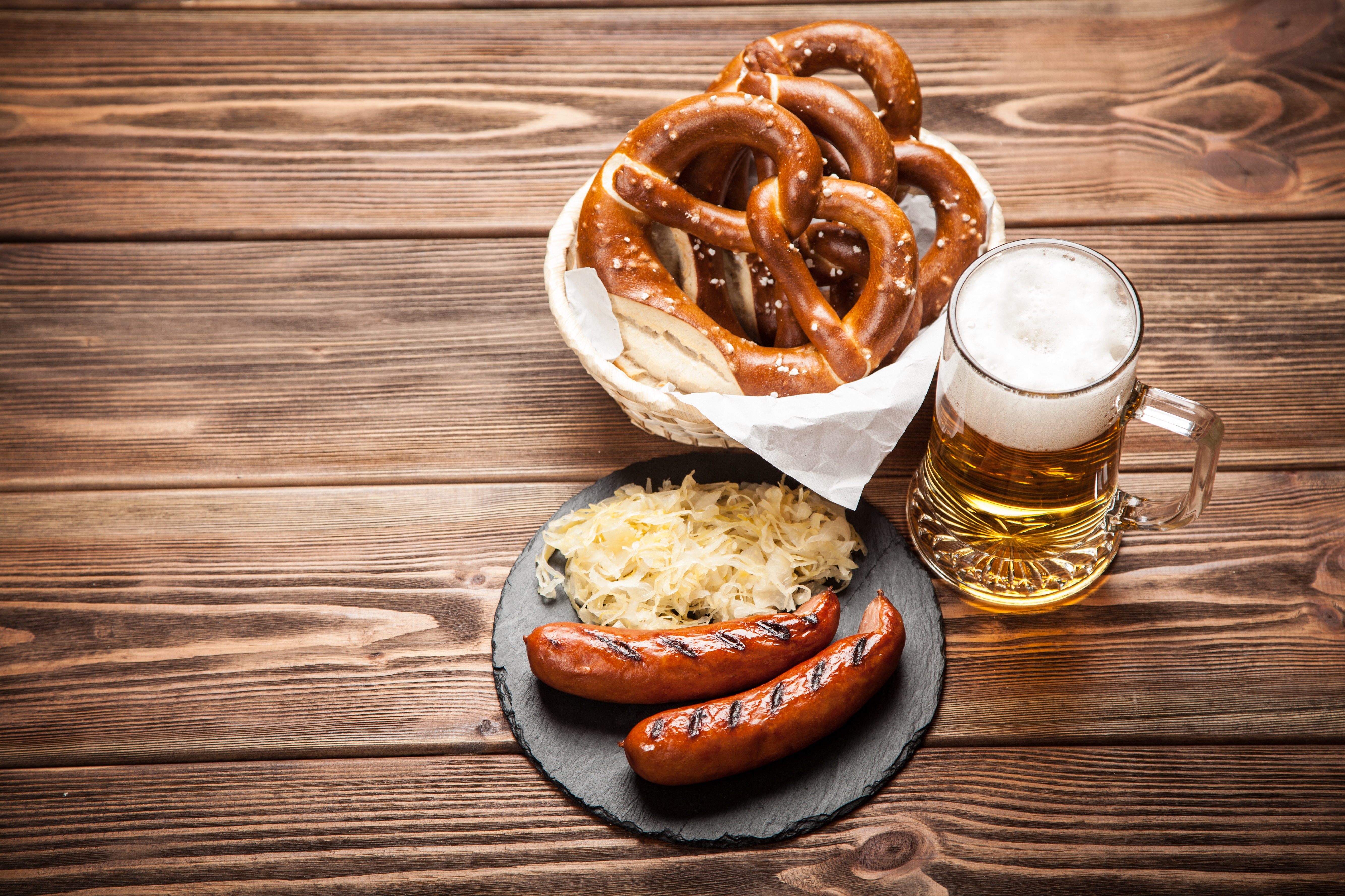 Traditional german food of pretzels, sauerkraut, bratwurst and beer on wooden table