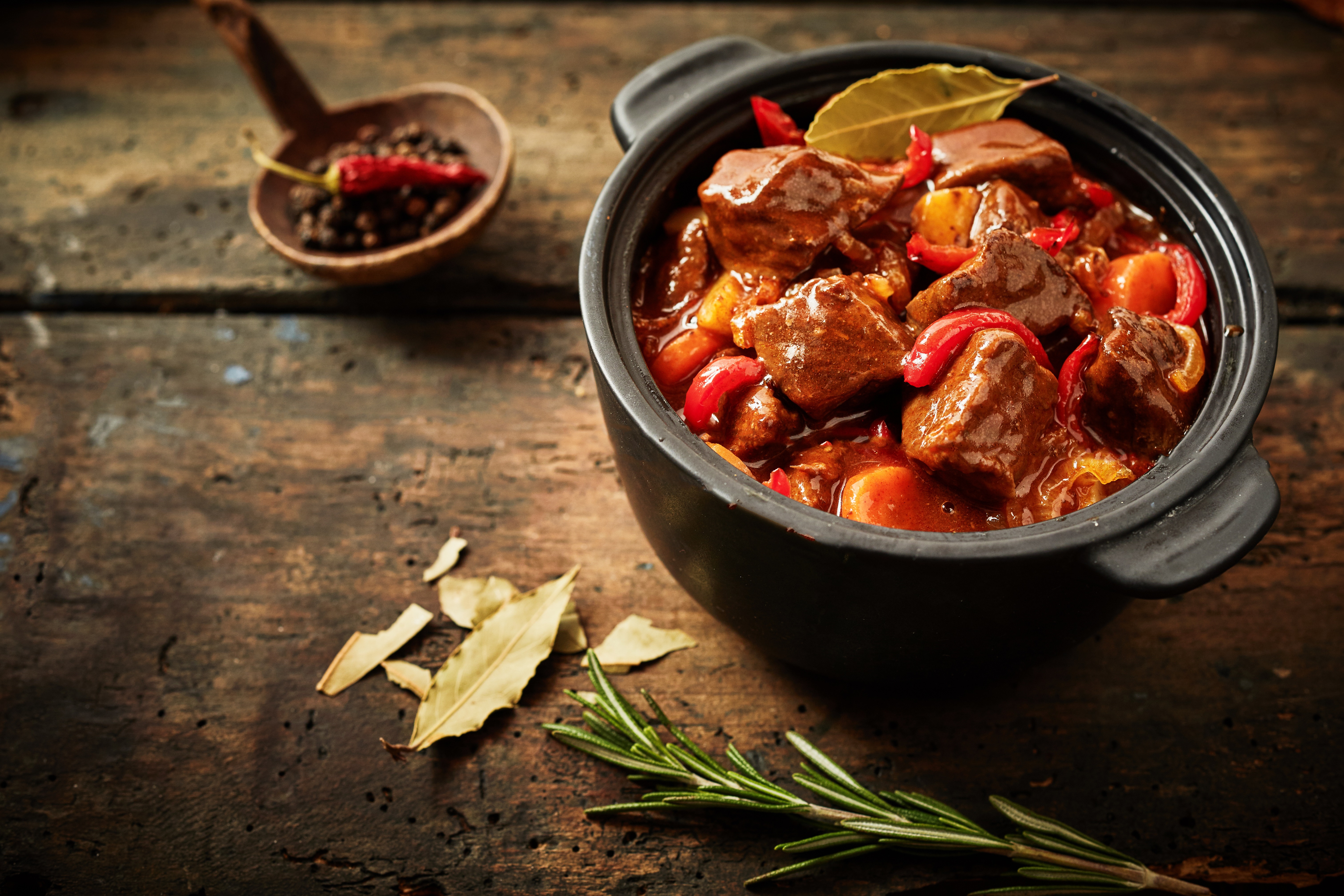 Pot of hungarian goulash on rustic wood background with chili peppers and laurel and copy space