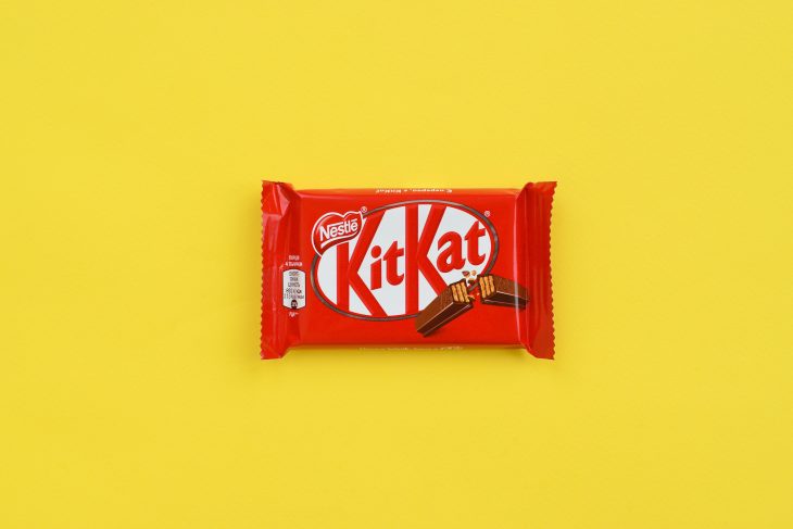 Kit Kat chocolate bar in red wrapping lies on yellow background