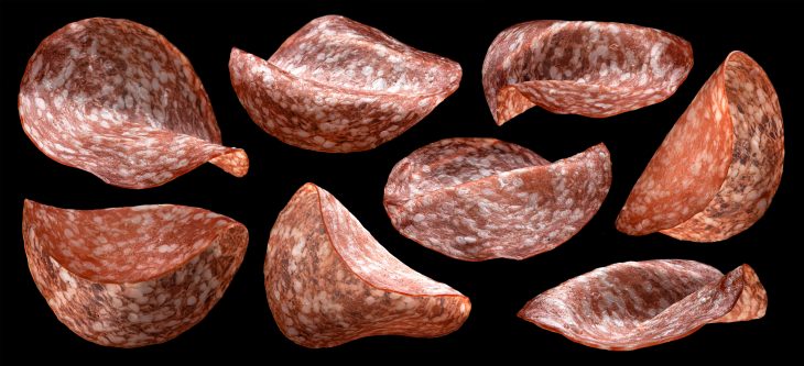 Thin salami smoked sausage slices on black background