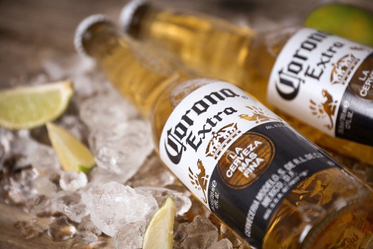 Two corona extra lager beer bottles on ice with lime slices on a rustic wooden table