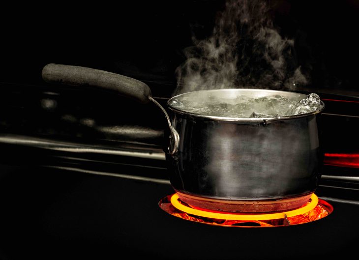 Horizontal shot of a boiling pot of water on a stovetop with a glowing red element.
