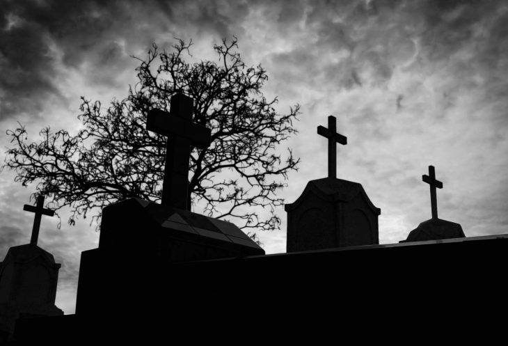 Cemetery or graveyard and dead tree in the night with dark sky and clouds. Silhouette death tree and cemetery. Funeral concept. Sadness, lament and death background. Scary and scary burial ground.