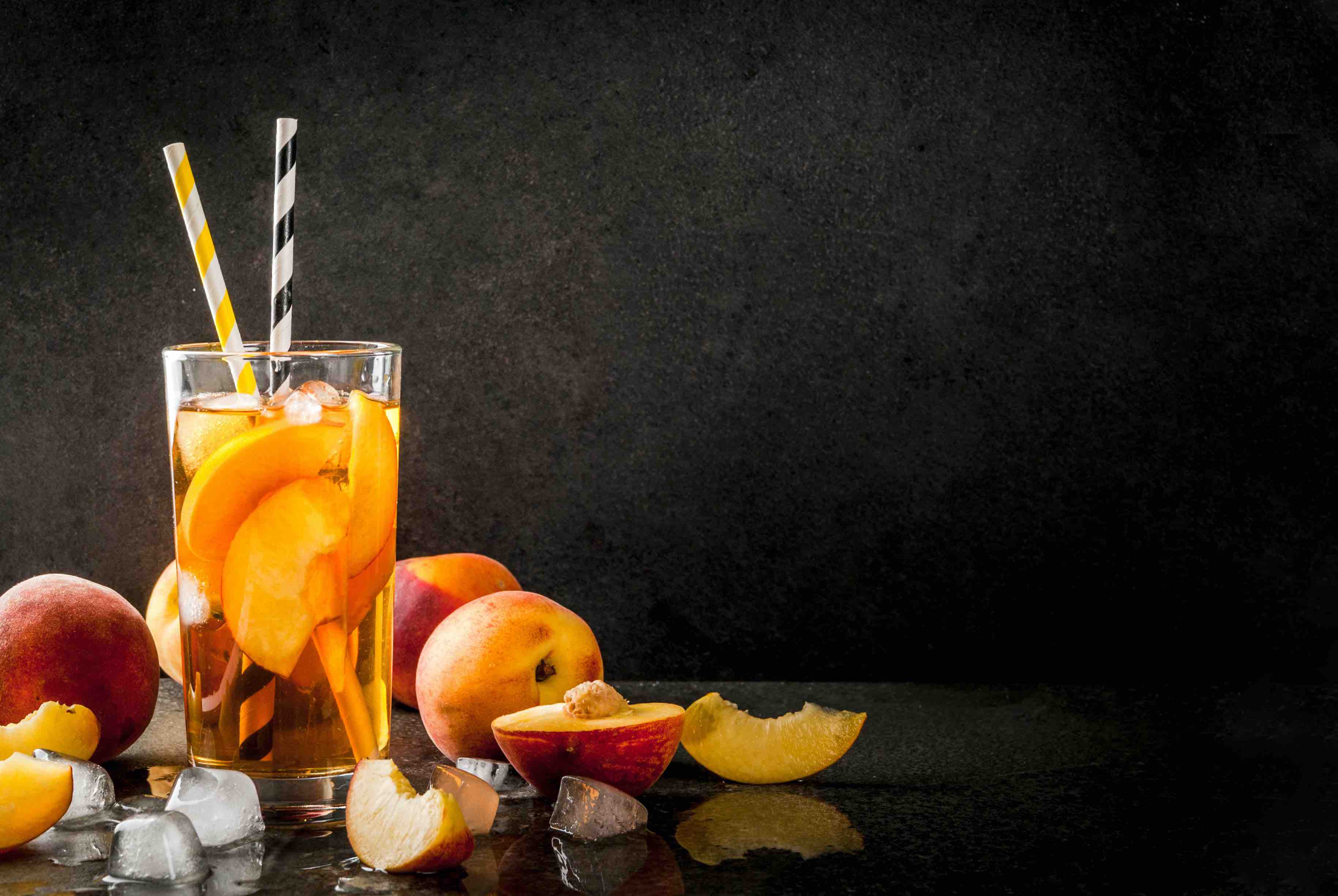 Summer refreshment drinks. Iced tea with pieces of organic home-made peach of nectarine. On a black stone background, with ice and ingredients. Copy space