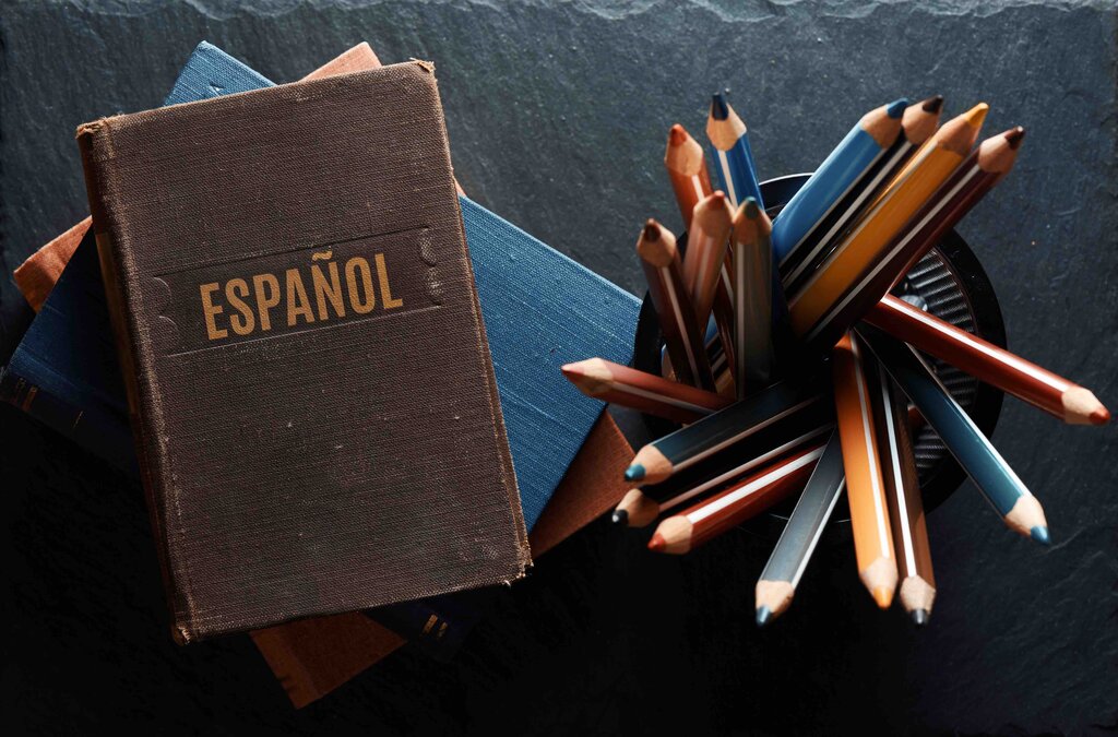 A flat lay shot of a and old leather book with the word espanol and a pen holder full of colorful pencils