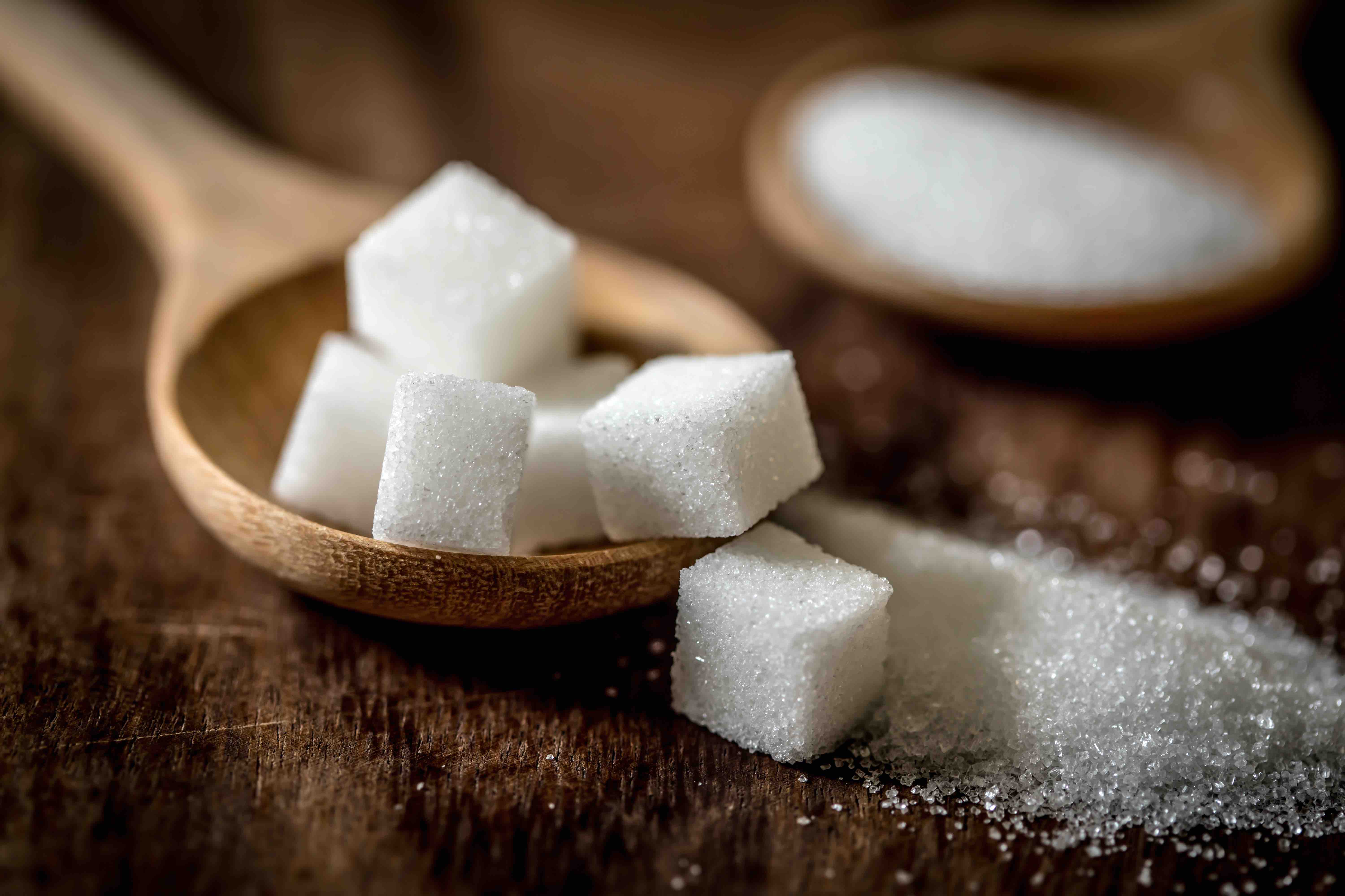 close up the sugar cubes and cane in wooden spoon on the table