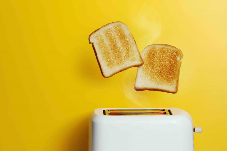 Slices of toast jumping out of the toaster against yellow background.