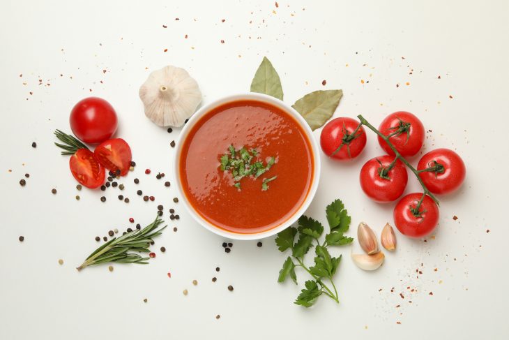 Bowl with tomato soup and ingredients on white background