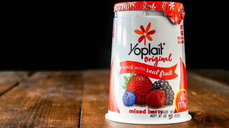 Yoplait original yogurt with nixed berry in plastic container on wooden table near window