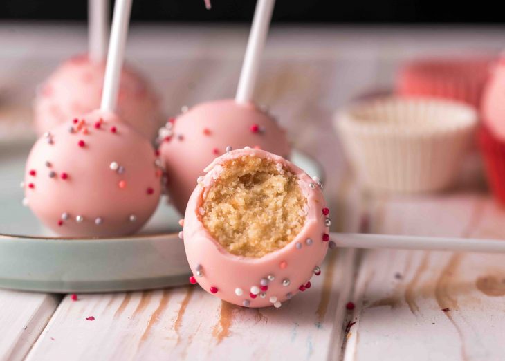 The pastry chef decorates cake pops with satin ribbons. Desserts with pink cream.