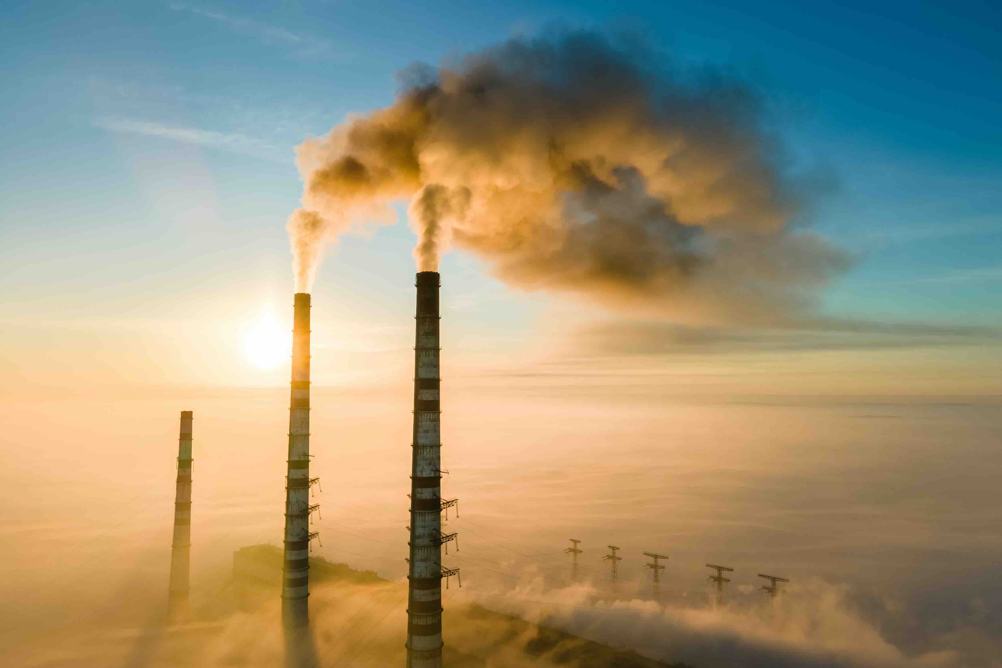 Aerial view of coal power plant high pipes with black smoke moving up polluting atmosphere at sunrise.