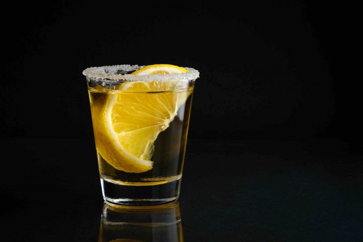 A shot glass of tequila with salt and lime with black isolated background