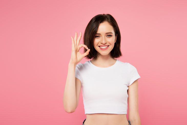 smiling pretty girl showing okay sign isolated on pink