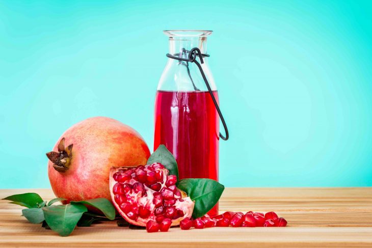 fresh red pomegranate juice with pomegranate seed and fruit with leaf on wooden table and blue background , healthy drink .