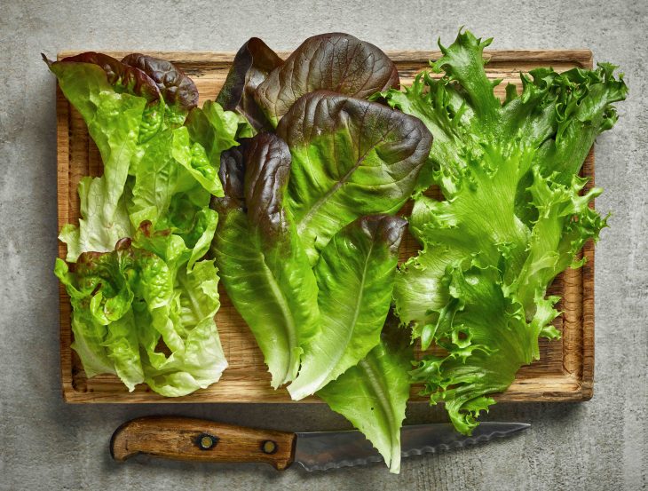 various kinds of lettuce on wooden cutting board, top view