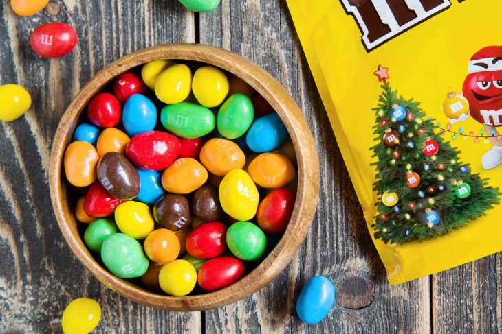 Peanut M&M's chocolate candy in a bowl and christmas bag on wooden background. Moscow - October 19, 2019