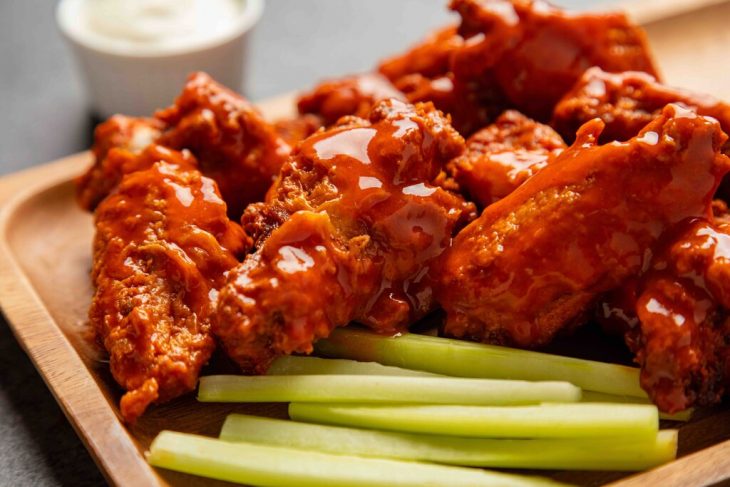 traditional Buffalo style chicken wings on a wooden plate with celery and ranch dressing