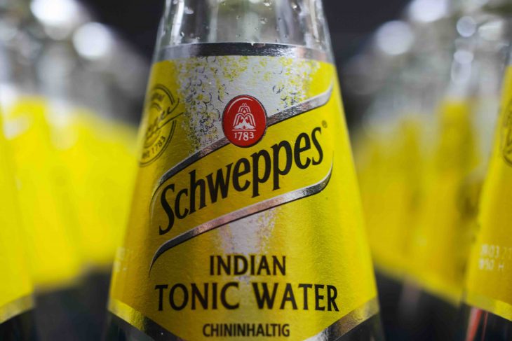 Close up of yellow Schweppes Indian tonic water bottle in container (selective focus on center)