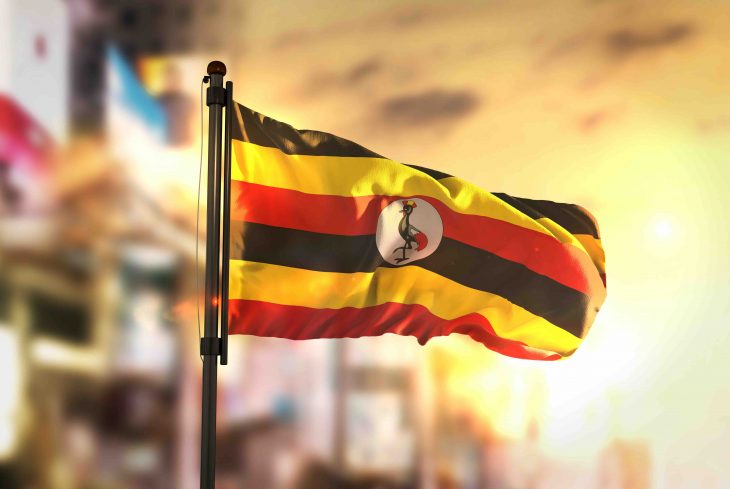 Uganda Flag Against City Blurred Background At Sunrise Backlight