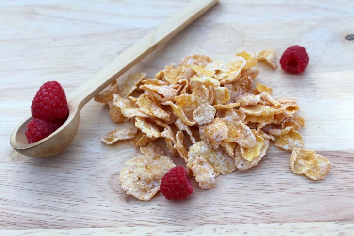 Fresh raspberries and frosted cereal on wood board
