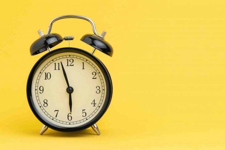 Alarm clock at almost 6 o'clock in the morning on yellow background with copy space using as business reminder, laziness or timer and deadline concept.