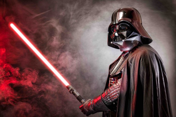 Portrait of Darth Vader costume replica with his sword . Lord Fener is a fictional character of Star Wars saga. Red grazing light and smoke