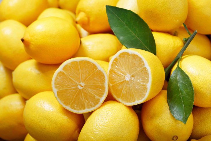 fresh lemons with leaves as background, top view