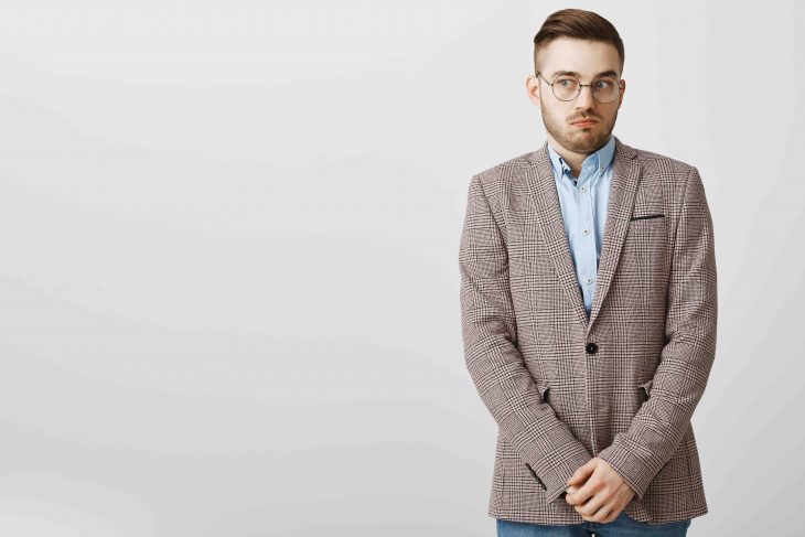 Intense worried european male employee feeling awkward and confused making mistake being scolded by boss feeling discomfort being in uncomfortable situation holding hands near pants and gazing aside.