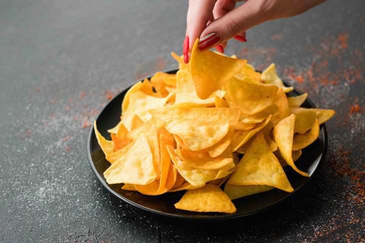 tortilla nacho chips food recipe. woman hand taking a slice of natural fried crisps of a plate